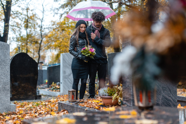 Пара, оплакивающая умершего любимого человека на кладбище осенью
 - Фото, изображение