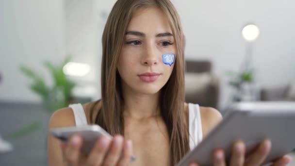 Portrait of young attractive woman with painted message box on her face holding phone and tablet in hands and smiling looking at the camera. Social media concept. Addiction to gadgets - Materiaali, video