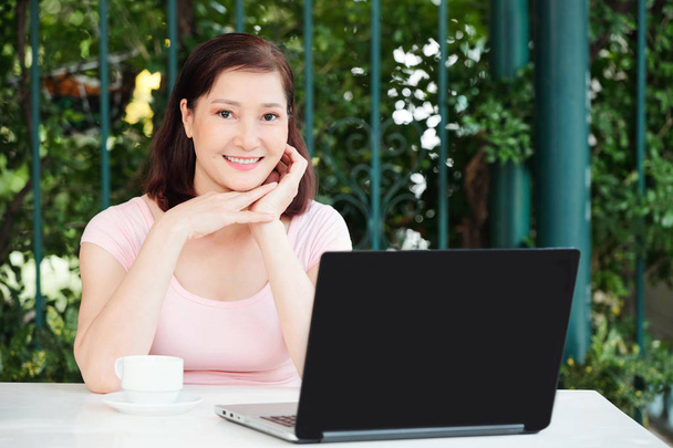Portret van positieve volwassen Vietnamese vrouwelijke digitale Nomad zittend in outdoor café en werken op laptop - Foto, afbeelding