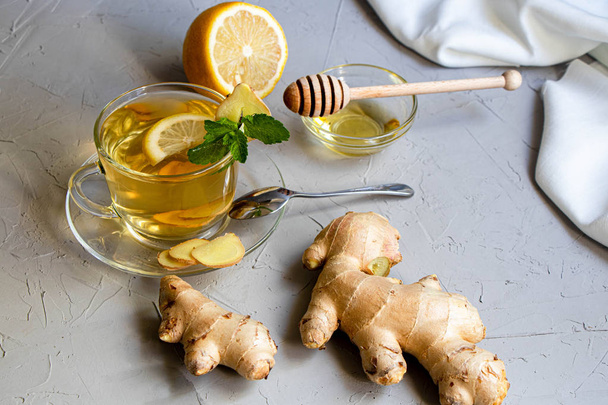 Ginger tea with lemon. Promotes weight loss. Heals colds. Nearby lies a fresh root and lime green.  - Photo, Image
