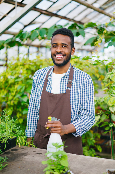Portrait of African American man farmer holding sprinkler in greenhouse smiling - Fotó, kép