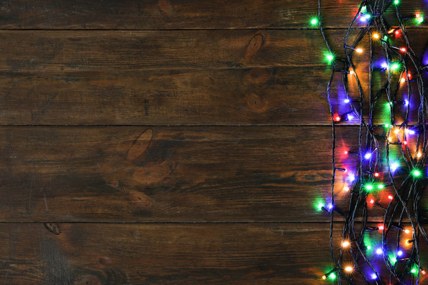 Ragyogó karácsonyi fények a barna fa háttér, felülnézet. Szóköz a szöveghez - Fotó, kép