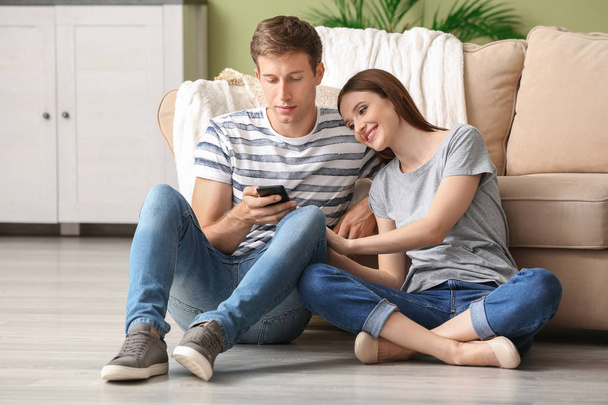 Νεαρό ζευγάρι με κινητά τηλέφωνα που χαλαρώνουν στο σπίτι - Φωτογραφία, εικόνα
