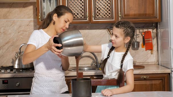 Mom and daughter are cooking a sponge cake together in the kitchen at home. - Zdjęcie, obraz
