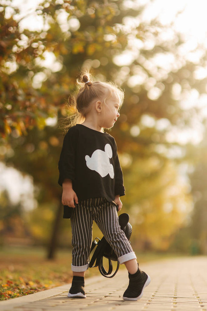 Ευτυχισμένο κοριτσάκι που περπατάει στο πάρκο το φθινόπωρο. Όμορφο θηλυκό παιδί σε κίτρινο φόντο - Φωτογραφία, εικόνα