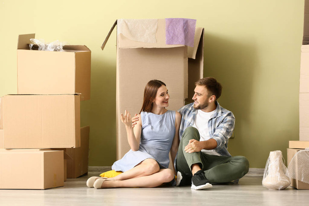 Happy young couple with belongings sitting on floor in their new house - Photo, Image