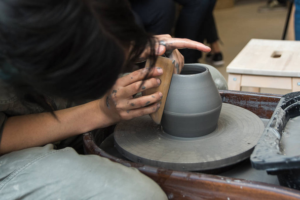 Auf einer Töpferscheibe stellt der Meister Produkte aus grauem Ton her. Mädchen schafft eine Keramikvase - Foto, Bild