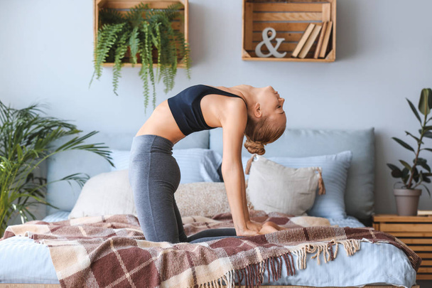 Молодая женщина практикует йогу на кровати дома
 - Фото, изображение