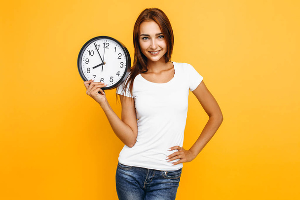 Young attractive woman with a watch on a yellow background - Photo, Image