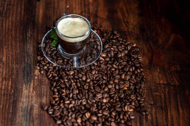 Una taza de delicioso café aromático. Está sobre un sustrato de granos de café. Tiene una espuma exuberante y blanca. Decorado con hojas de menta
.  - Foto, Imagen