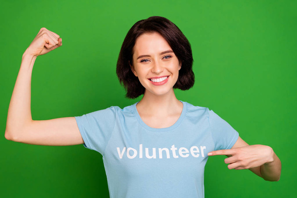 Close-up portrait of her she nice attractive cheerful cheery content girl wearing blue t-shirt demonstrating pointing at arm muscles isolated over bright vivid shine vibrant green background - Foto, immagini
