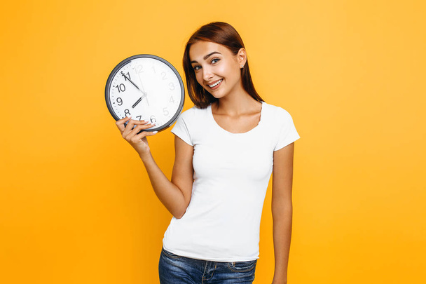 Young attractive woman with a watch on a yellow background - Foto, immagini