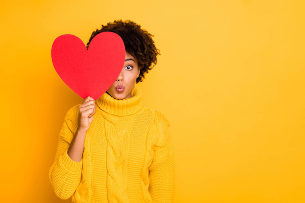 Photo of curly wavy brown haired afro girlfriend peeking out of big red heart to kiss you through air wearing yellow pullover isolated over vibrant color background - Valokuva, kuva