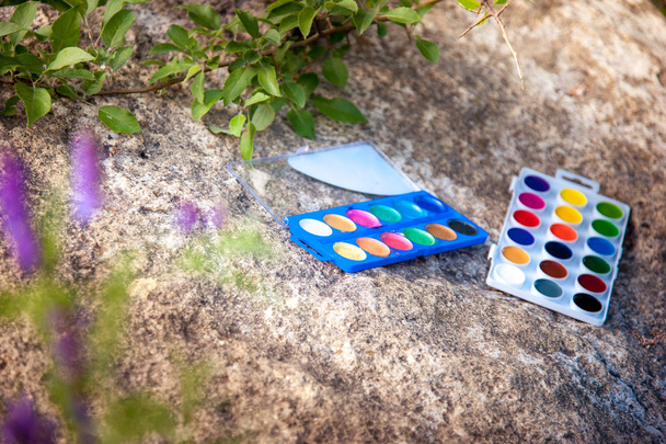 watercolor paints lie on a large stone in nature - Foto, afbeelding
