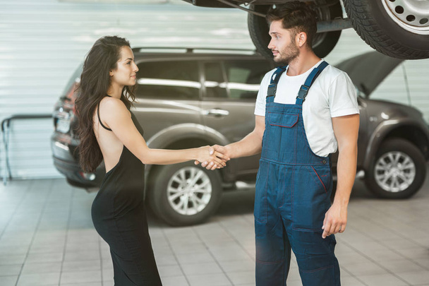 young handsome mechanic and beautiful woman client shaking hands in gratitude for great service provided - Foto, imagen
