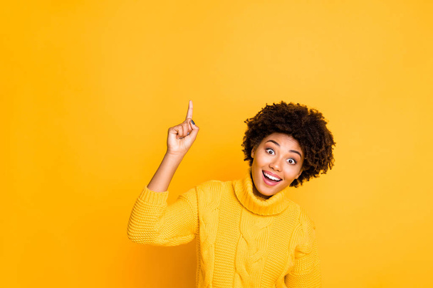 Photo of dark skin funny lady indicating finger up empty space on sale placard wear warm knitted jumper isolated yellow background - Foto, afbeelding