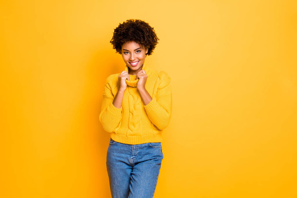Photo of dark skin funny lady in good mood holding hands big collar of warm knitted pullover isolated yellow color background - Fotoğraf, Görsel