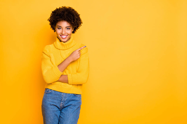 Photo of dark skin lady indicating finger empty space wear warm knitted pullover and jeans isolated yellow background - Fotografie, Obrázek