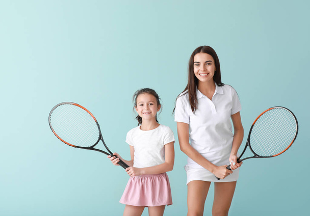 Little girl and her mother with tennis rackets on color background - Photo, Image