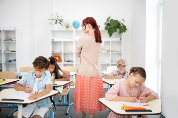 Nauczyciel chodzenia między biurami podczas pisania testu dzieci - Zdjęcie, obraz