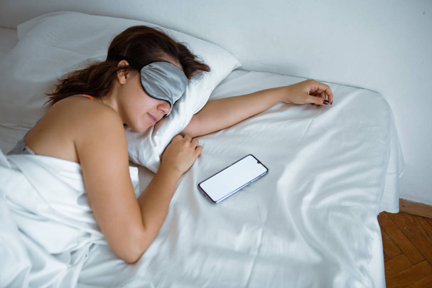 mujer durmiendo en el teléfono inteligente máscara de sueño cerca de ella
 - Foto, Imagen