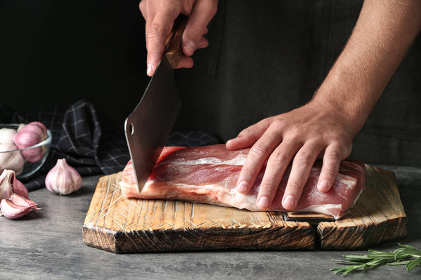 Man cutting fresh raw meat on table against dark background, closeup - Fotografie, Obrázek