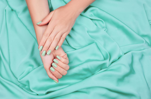 Hands of a young girl on a mint silk cloth, manicure on a trendy background , green polish. - 写真・画像