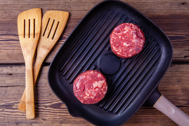 Top view of two raw beef burger meats on grill pan on a wooden background - Fotó, kép