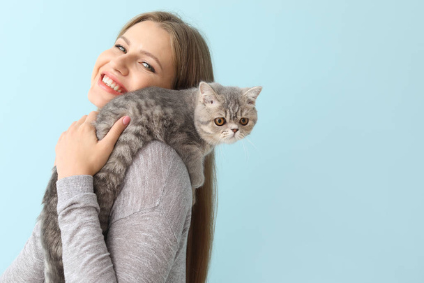 Beautiful young woman with cute cat on color background - Foto, imagen