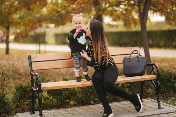 Szczęśliwa matka i jej córka gra w jesiennym parku. Rodzina, koncepcja stylu życia. Czas jesienny. Matka i córka siedzi na ławce - Zdjęcie, obraz