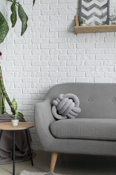 Morbido divano con cuscino elegante vicino al muro di mattoni bianchi in camera
 - Foto, immagini