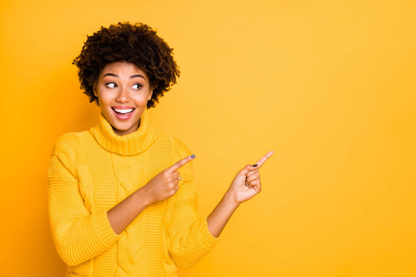 Photo of dark skin lady indicating fingers empty space on low prices placard wear warm knitted pullover isolated yellow color background - 写真・画像