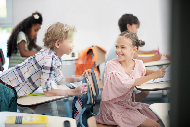 fröhliches Mädchen in rosa Kleid lächelt, während es mit Klassenkameradin spricht - Foto, Bild