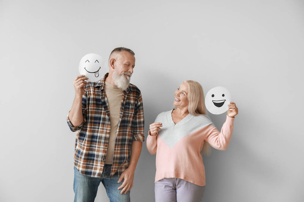 Happy mature couple with emoticons against light background - Foto, Imagen