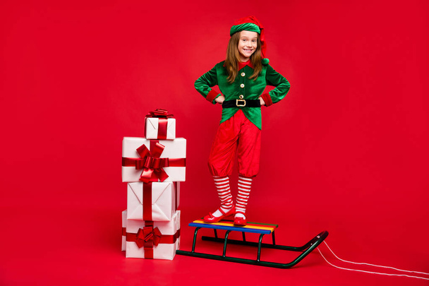 Full length body size view of nice attractive cheerful cheery glad funny pre-teen elf standing on sled fairy miracle winter tradition isolated over bright vivid shine red background - Foto, afbeelding