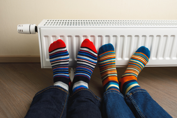 πόδια με πολύχρωμες κάλτσες μπροστά από το καλοριφέρ θέρμανσης - Φωτογραφία, εικόνα