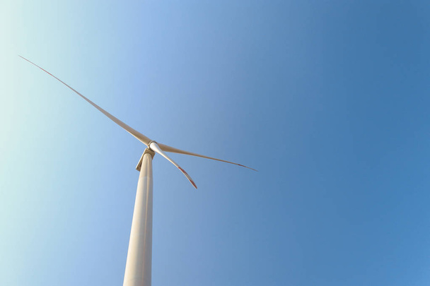 Looking upward to a big wind turbine and a blue sky. Alternative energy source, production and power generation. Ecology and freedom concept - Photo, Image