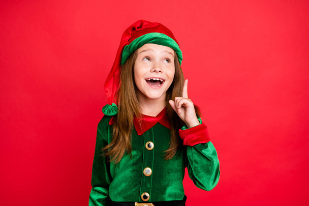 Portrait of surprised liitle kid elf raising her index finger having solution screaming wow omg wearing greem elf costume hat cap isolated over red background - Photo, image