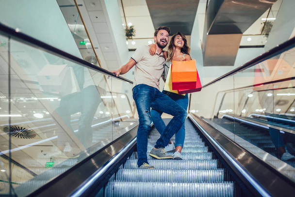 Szczęśliwa Młoda para z torby na zakupy dzieje w dół przez schody ruchome - Zdjęcie, obraz