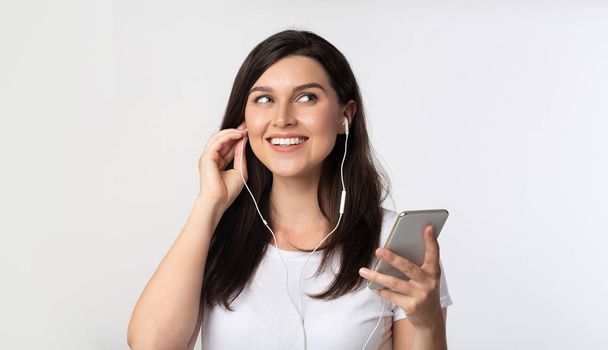 Girl Holding Smartphone Enjoying Song In Earphones, White Background - Foto, Imagen