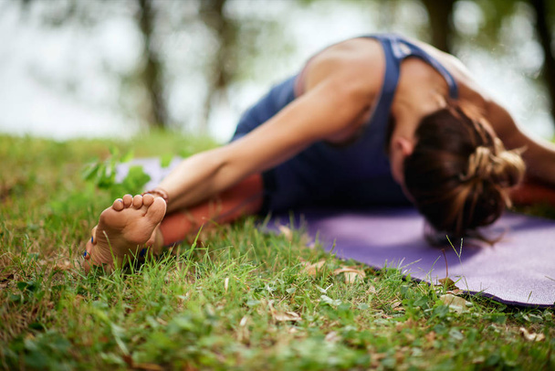 Toegewijde blanke vrouw zittend op mat in de natuur in de buurt van water en zittend breed legged voorwaarts Bend Yoga pose. - Foto, afbeelding