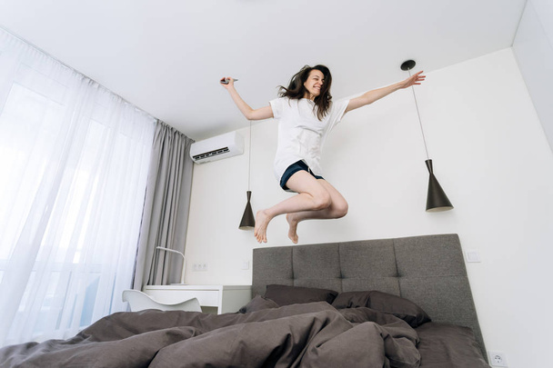 Молодая взрослая женщина просыпается и прыгает в постель со смартфоном
 - Фото, изображение