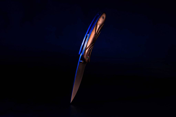 Black knife on a black background. Multi-colored light on the knife. - Photo, Image