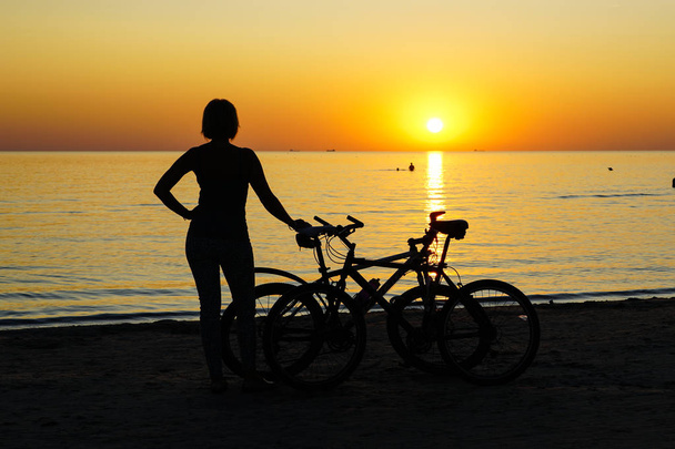 silueta de mujer con bicicleta al atardecer junto al mar
 - Foto, imagen