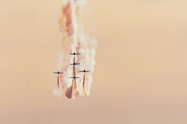 Groupe d'avions de chasse volant contre un ciel orange vif, effectuant des figures de la traînée de fumée
. - Photo, image