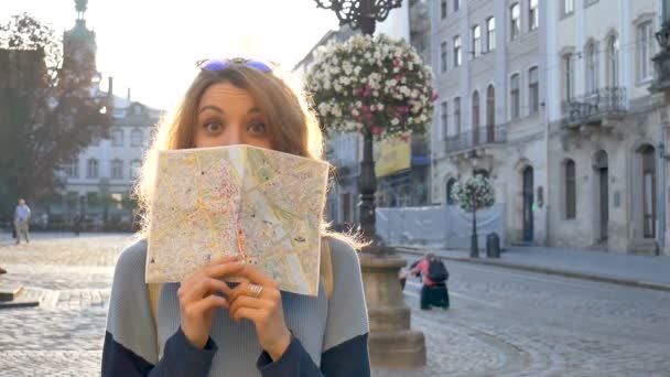 Gelukkig opgewonden volwassen meisje kijkt naar de papieren kaart en op zoek naar richting vroeg in de ochtend in de oude Europese stad op een leeg plein - Video