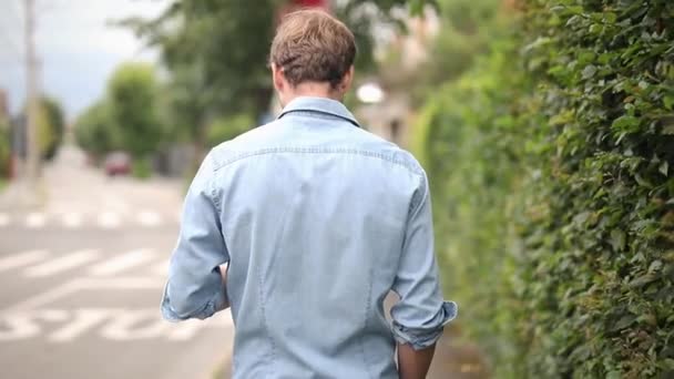 telefonuna mesaj alan yürüyen bir adamın arka görünümü ve sokaktaki birine merhaba demek için döner - Video, Çekim
