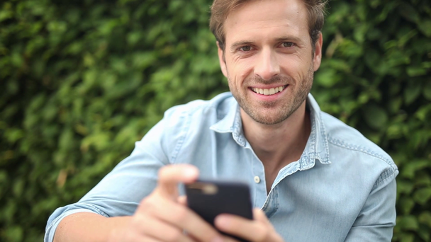 zbliżenie zwykłego mężczyzny pracując na swoim telefonie komórkowym i uśmiechem - Materiał filmowy, wideo