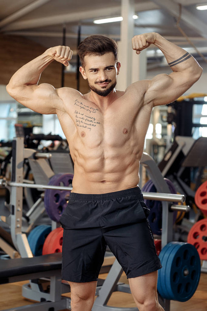 Handsome muscular athletic young man bodybuilder fitness model show his biceps after exercises in gym. - Zdjęcie, obraz