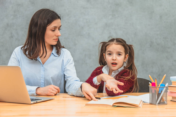 Young mother and schoolgirl on a gray background. Mom shows the daughter the task. During this, the girl is confused. On a gray background. - 写真・画像